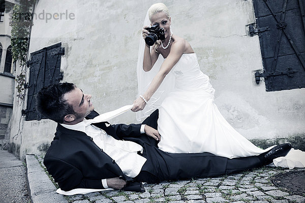 Braut fotografiert Bräutigam  der am Boden liegt  Fotoshooting  Hochzeit