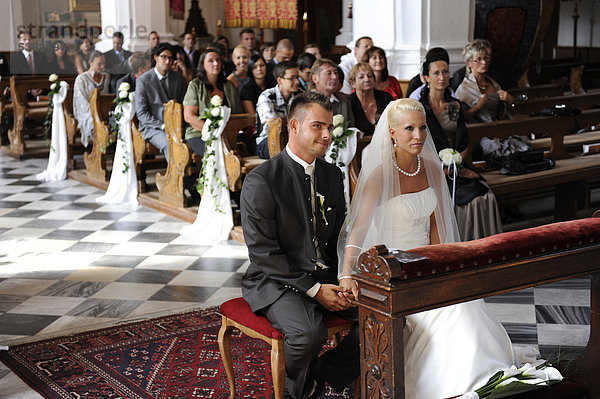 Brautpaar sitzt in der Kirche vor der Hochzeitsgesellschaft