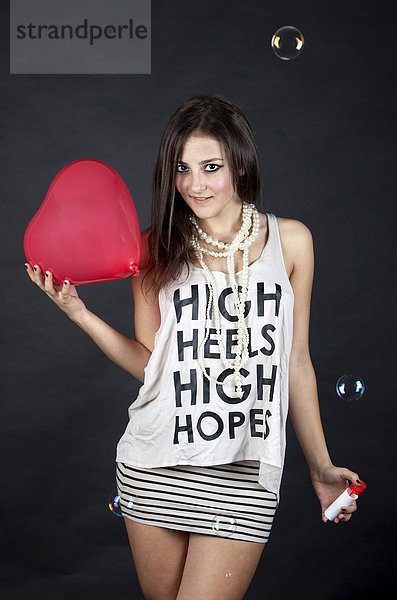 Junge Frau mit Herzballon  Seifenblasen und Top mit der Aufschrift High heels  high hopes