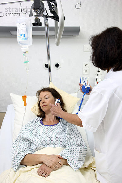 Krankenschwester misst einer Patientin im Krankenbett mit einem digitalen Fieberthermometer die Körpertemperatur  Krankenhaus