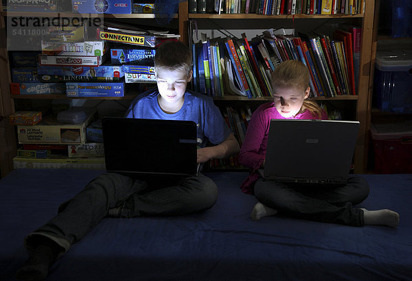 Geschwister  Junge  12 Jahre  und Mädchen  10 Jahre  spielen in ihrem Spielzimmer auf 2 Laptop Computern ein Computerspiel gegeneinander