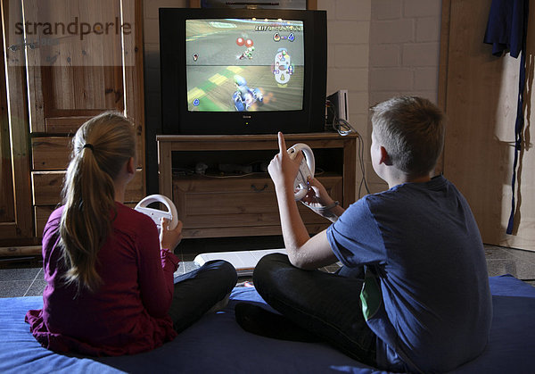 Geschwister  Junge  12 Jahre  und Mädchen  10 Jahre  spielen in ihrem Spielzimmer gemeinsam ein Computerspiel  Wettrennen  Autorennen  Wii Spielekonsole