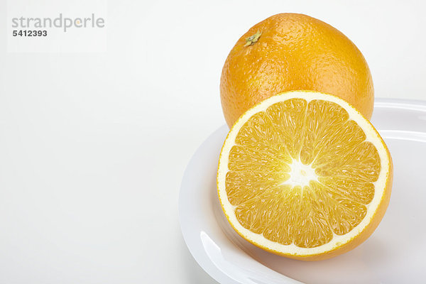 Zwei Orangen (Citrus sinensis)  eine ganze und eine halbe  auf einem weißen Teller