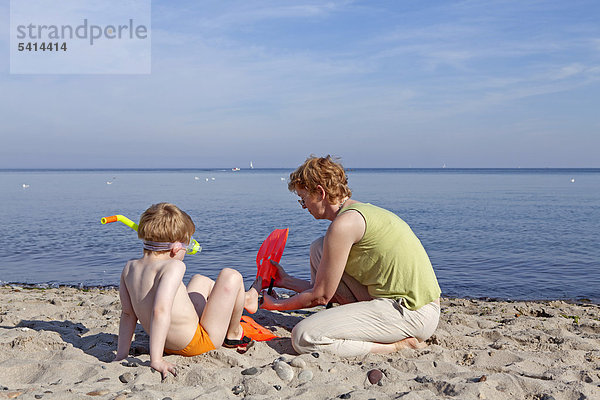 Mutter hilft ihrem Sohn beim Anziehen der Schwimmflossen  Strand  Kühlungsborn  Mecklenburg-Vorpommern  Deutschland  Europa