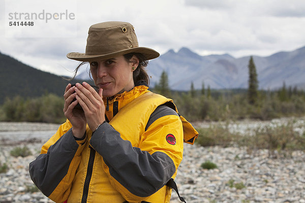 Junge Frau trinkt  genießt eine Tasse Tee  Wind River  Peel Watershed  hinten die nördlichen Mackenzie Mountains  Yukon Territory  Kanada