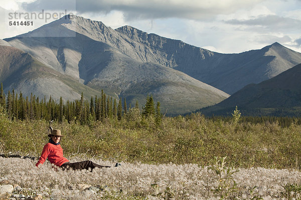 Junge Frau entspannt  genießt  sitzt inmitten von Wollgras im Abendlicht  Wind River  Yukon Territory  Kanada