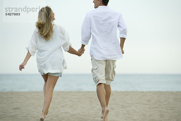 Paar geht Hand in Hand am Strand  Rückansicht