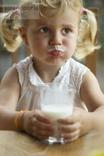 Kleines Mädchen mit Milchschnurrbart genießt ein Glas Milch