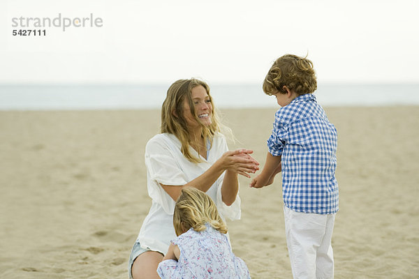 Mutter und Kinder spielen im Klang am Strand