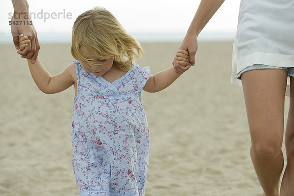 Kleines Mädchen  das Hand in Hand mit den Eltern am Strand spazieren geht.