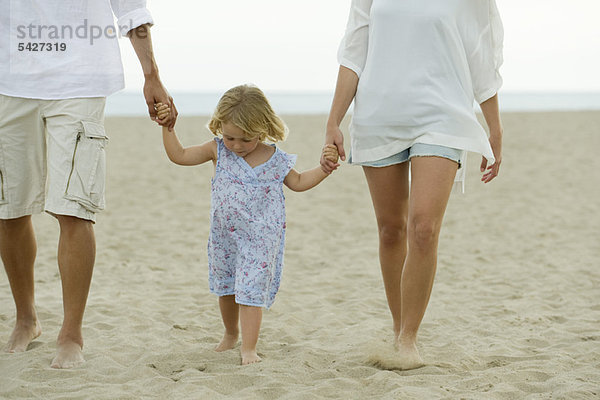 Kleines Mädchen  das mit seinen Eltern am Strand spazieren geht.