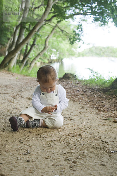 Kleines Mädchen sitzend auf Feldweg im Wald