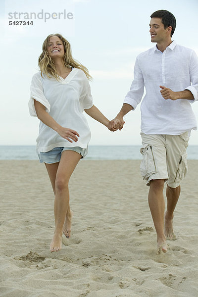 Paar geht Hand in Hand am Strand spazieren