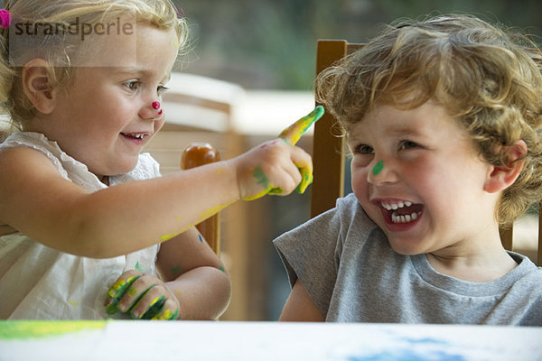 Kleines Mädchen wischt Farbe auf die Nase ihres Bruders.