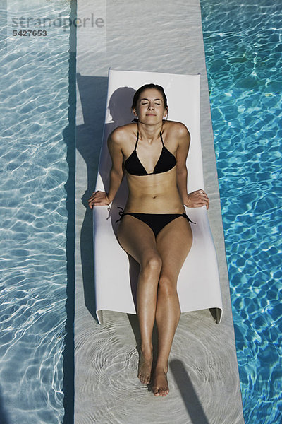 Junge Frau beim Sonnenbaden auf dem Liegestuhl am Pool