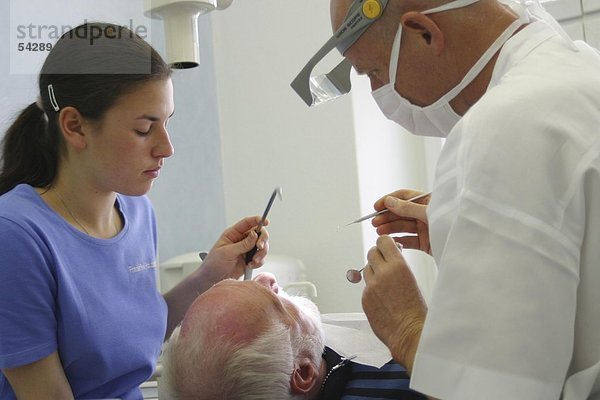 Zahnarzt kontrolliert mit Assistentin Zahnstein am Patienten