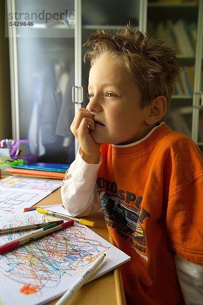 Unruhiger Junge sitzt abwesend vor dem Schreibtisch - ADHS Syndrom
