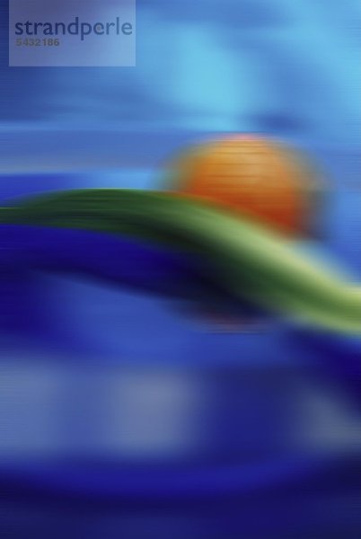 unscharfe Fotografie einer orangenen Kugel die mit einem grünen Blatt im Wasser schwimmt