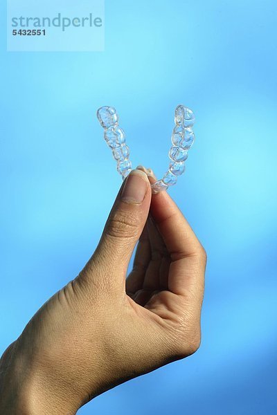 Bruxismus - bruxism - das meist unbewusste nächtliche Knirschen mit den Zähnen - durch das Knirschen mit den Zähnen treten in den meisten Fällen Fehlbelastungen der Zähne bzw. Zahngruppen oder Kiefergelenksbeschwerden auf - um eine Entlastung der Zähne und eine Gelenkschonung bei Kieferarthropathie zu erreichen wird eine individuell angepasste Kunststoffplatte   Knirscherschiene   Aufbissbehelf ( Okklusionsschiene oder Relaxierungsschiene ) für den Patienten angefertigt - diese sollte vorwiegend nachts getragen werden - Ursachen können psychischer ( Stress )   physischer ( Skeletterkrankungen ) oder neurologischer ( MS Multiple Sklerose ) Natur sein - eine Frau hält eine Knirscherschiene für den Unterkiefer zwischen den Fingern