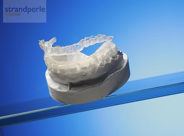 Beißschienen für Oberkiefer und Unterkiefer auf Gipsmodell vor blauem Hintergrund ( Orthoarch - lat.) - Bruxismus - bruxism - das meist unbewusste nächtliche Knirschen mit den Zähnen - durch das Knirschen mit den Zähnen treten in den meisten Fällen Fehlbelastungen der Zähne bzw. Zahngruppen oder Kiefergelenksbeschwerden auf - um eine Entlastung der Zähne und eine Gelenkschonung bei Kieferarthropathie zu erreichen wird eine individuell angepasste Kunststoffplatte   Knirscherschiene   Aufbissbehelf ( Okklusionsschiene oder Relaxierungsschiene ) für den Patienten angefertigt - diese sollte vorwiegend nachts getragen werden - Ursachen können psychischer ( Stress )   physischer ( Skeletterkrankungen ) oder neurologischer ( MS Multiple Sklerose ) Natur sein