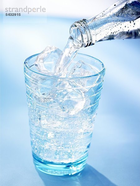 Wasser wird aus einer Flasche in ein Glas mit Eiswürfeln geschenkt. CO2 ( Wasser ) - H2O ( Kohlensäure )