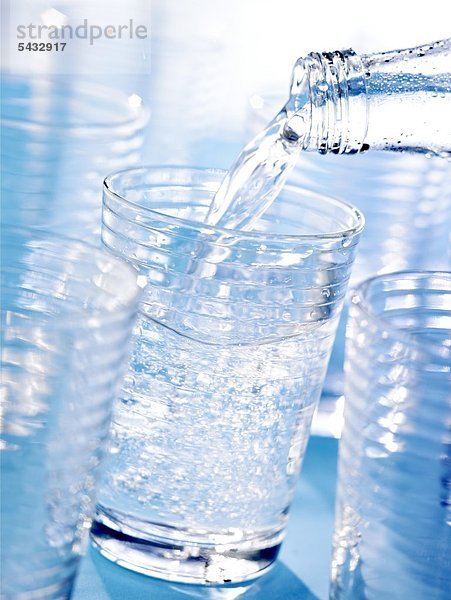 Viele Gläser vor blau - in eines wird aus einer Flasche Wasser gefüllt. CO2 ( Wasser ) - H2O ( Kohlensäure )