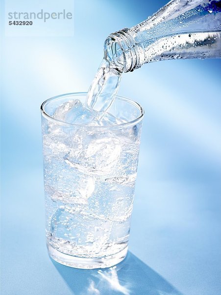 Wasser wird aus einer Flasche in ein Glas mit Eiswürfeln geschenkt. CO2 ( Wasser ) - H2O ( Kohlensäure )