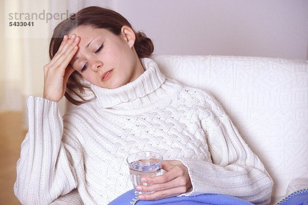 Junge Frau mit Erkältung auf Sofa   hält Wasserglas