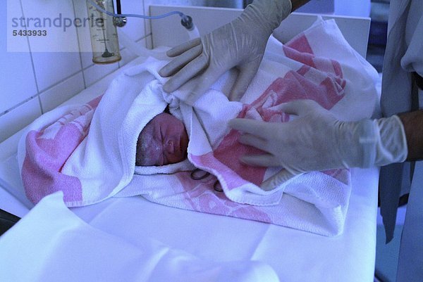 Neugeborenes direkt nach der Geburt   gehalten von einer Pflegerin und in ein Handtuch eingewickelt -