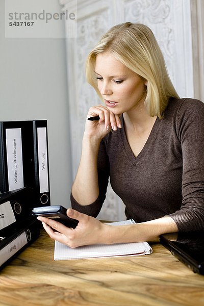 Ernste blonde Frau schaut auf einen Taschenrechner