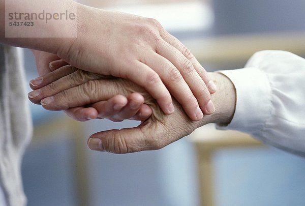 Nahaufnahme - Hände einer Pflegerin halten die Hand einer alten Patientin