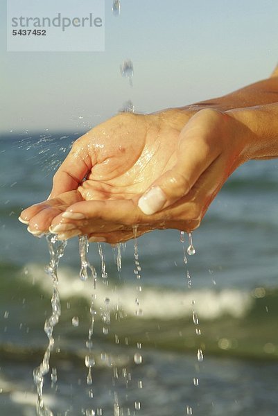 Zwei weibliche Hände schöpfen Wasser aus dem Meer   Tropfen fallen