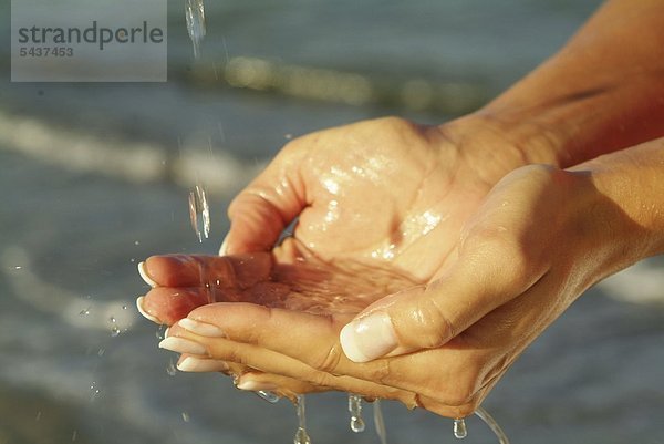 Zwei weibliche Hände schöpfen Wasser aus dem Meer   Tropfen fallen