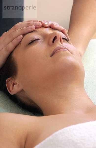 Eine Frau bekommt eine Massage am Kopf   die Frau hat die Augen geschlossen - Die Hände der Heilpraktikerin befinden sich seitlich an der Stirn -
