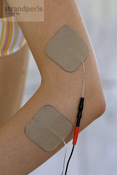 Junge Frau mit TENS-Elektroden zur Behandlung von Schmerzen bei einer Epicondylitis radialis/ulnaris - young woman with TENS electrodes to treat a tennis arm