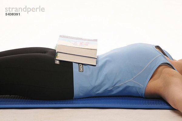 Bauchmuskeltraining und Stärkung der Zwerchfellatmung - Junge Frau in Gymnastikkleidung liegt auf einer Gymnastikmatte - Bücher auf Ihrem Bauch dienen als Gewichte