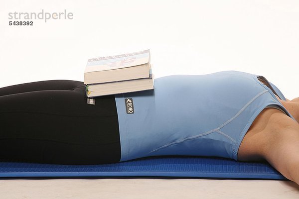 Bauchmuskeltraining und Stärkung der Zwerchfellatmung - Junge Frau in Gymnastikkleidung liegt auf einer Gymnastikmatte - Bücher auf Ihrem Bauch dienen als Gewichte