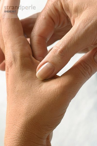 Nahdetail - Junge Frau massiert die Haut zwischen Daumen und Zeigefinger - Finger Akupressur