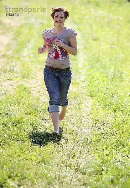 Junge Frau rennt lachend über die Wiese