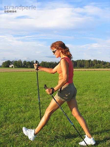 Eine Frau beim Nordic Walking geht quer über eine Wiese.