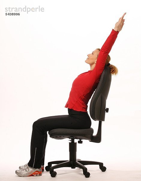 fit im Büro - junge Frau sitzt auf Bürostuhl und macht Gymnastik - Arme über den Kopf strecken - Beweglichkeit