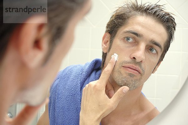 Mann steht vor dem Badezimmerspiegel und verwendet Gesichtscreme - man takes face cream