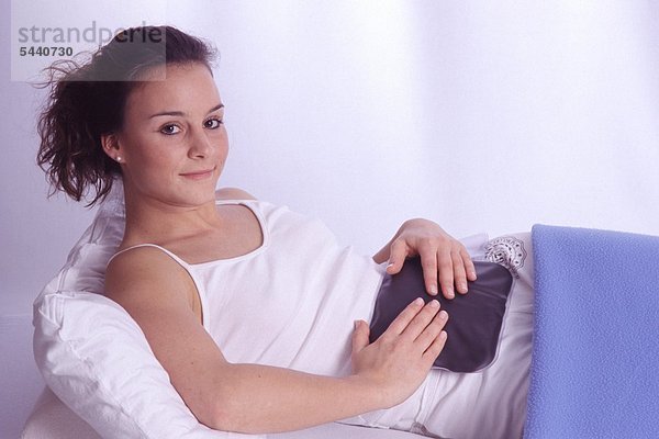 Junge Frau behandelt Bauchbeschwerden mit einem Moorkissen