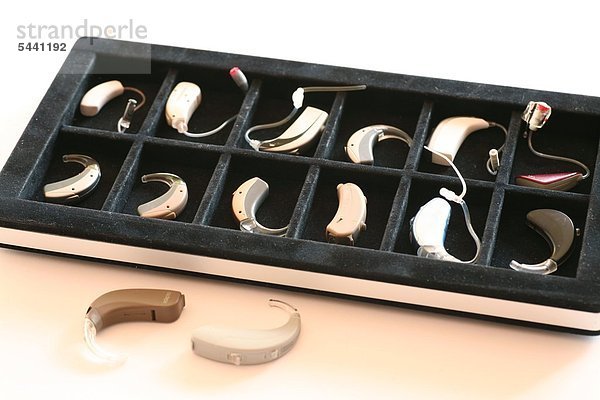 Freisteller - verschiedene kleine Hörgeräte in einem Etui und zwei Exemplare außerhalb auf weißem Untergrund