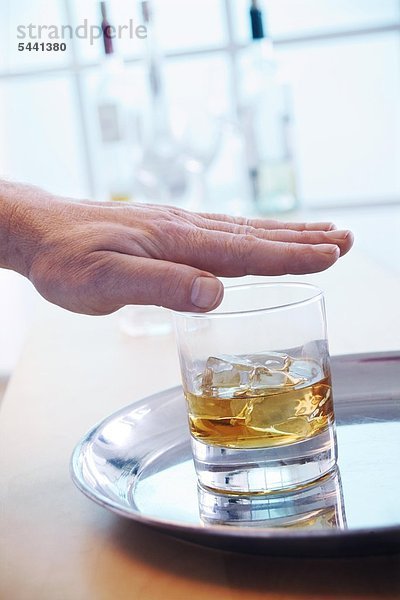 Männliche Hand über Whiskyglas