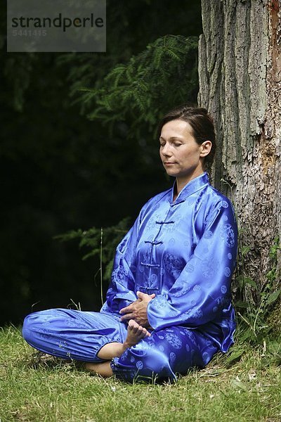 Chan Mi Qi Gong - Innere Lächeln -Frau im blauen Kimono in der Natur mach Entspannungsübung - gegen Verspannung und Fehlhaltung   Stress und Anspannung -innere Harmonie durch einen gestärkten Rücken -