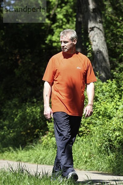 älterer Mann geht in Sportkleidung auf einem Waldweg spazieren