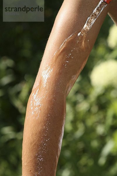 Kalter Armguss nach Kneipp - Junge Frau gießt an einem sonnigen Sommertag ihren Arm mit kaltem Wasser ab