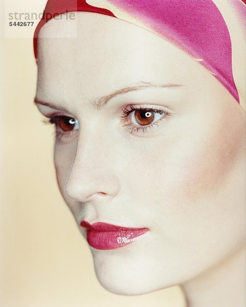 Portrait einer Frau mit farbigem Kopftuch auf beigem Hintergrund