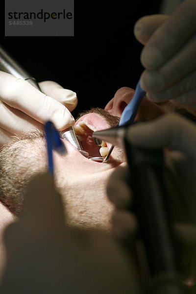 Zahnarztpraxis : Zahnarzt und Zahnarzthelferin behandeln einen Patienten mit Bohrer   Mundspiegel und Absauger